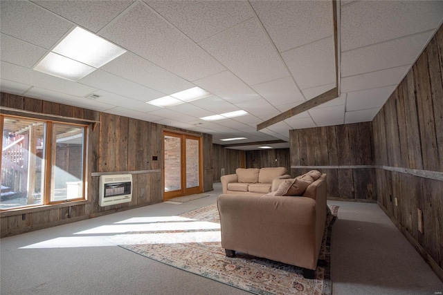 carpeted living room with a paneled ceiling, heating unit, and wood walls