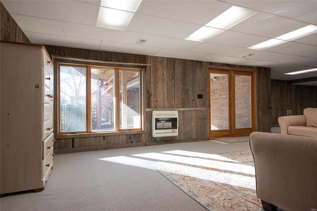 living room featuring heating unit, wooden walls, a drop ceiling, and carpet flooring