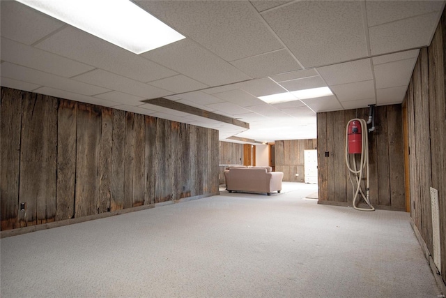 basement featuring light colored carpet, a drop ceiling, and wooden walls