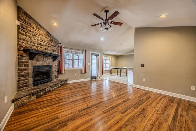 unfurnished living room featuring hardwood / wood-style flooring, ceiling fan, a stone fireplace, and vaulted ceiling