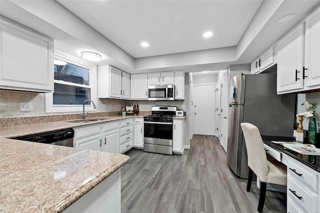 kitchen featuring sink, light hardwood / wood-style flooring, white cabinetry, stainless steel appliances, and tasteful backsplash