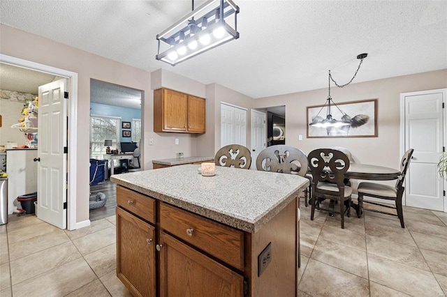 kitchen with light tile patterned flooring, a center island, a textured ceiling, and decorative light fixtures