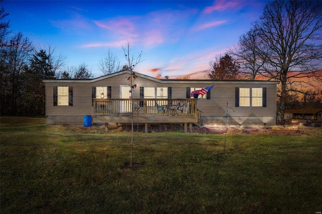 back house at dusk featuring a lawn and a deck