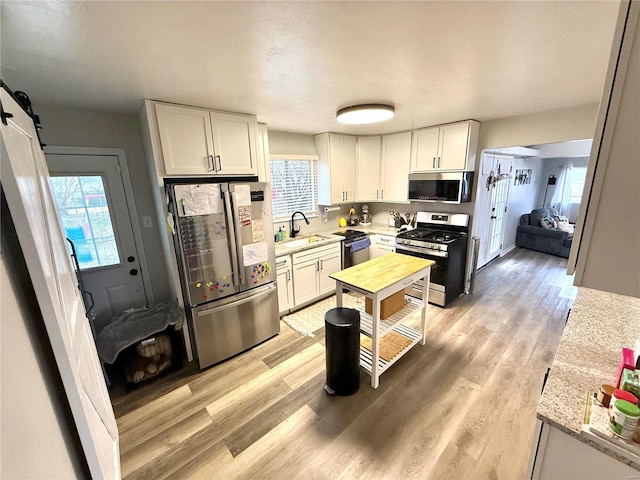 kitchen with sink, light wood-type flooring, stainless steel appliances, a barn door, and white cabinets