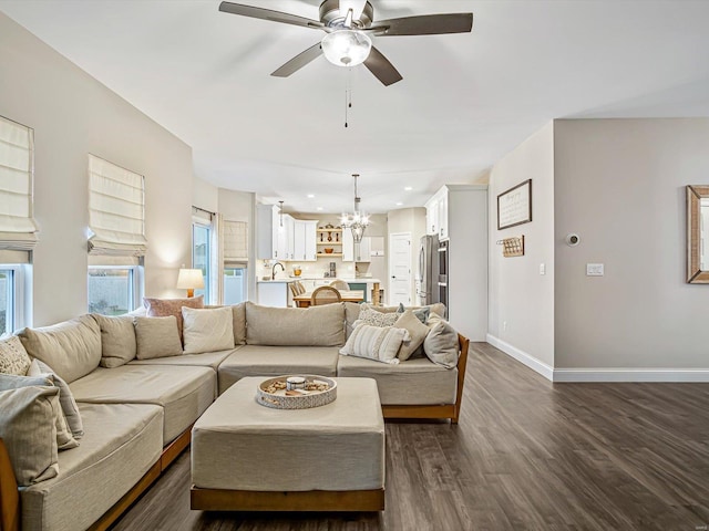 living area featuring ceiling fan with notable chandelier, dark wood finished floors, and baseboards