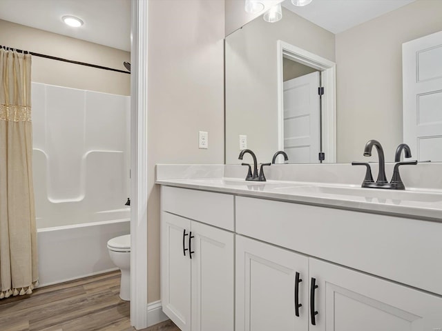 full bathroom with double vanity, toilet, wood finished floors, shower / bath combo with shower curtain, and a sink