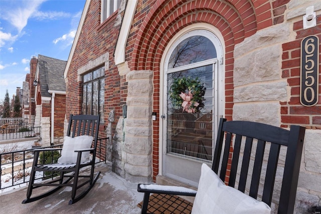 entrance to property with a shingled roof, covered porch, and brick siding