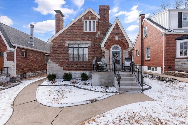 english style home featuring a chimney and brick siding