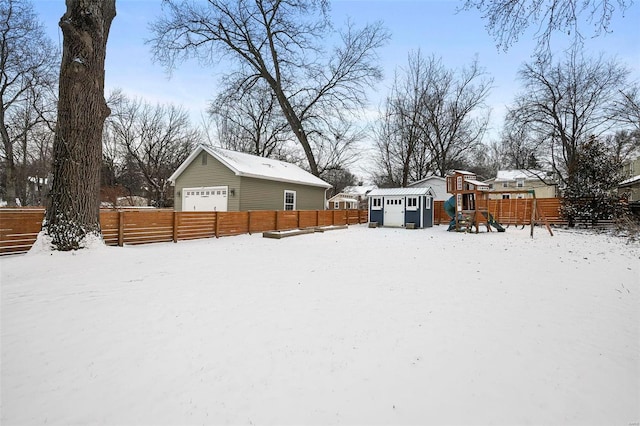 yard layered in snow featuring a shed, a playground, and a garage