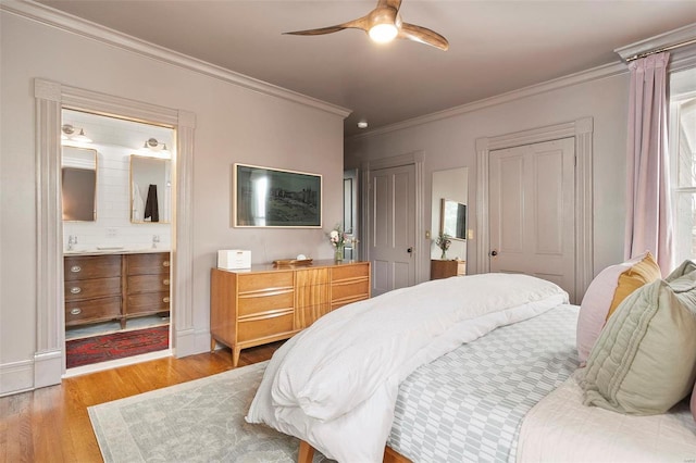 bedroom featuring ensuite bathroom, light hardwood / wood-style floors, ceiling fan, ornamental molding, and two closets