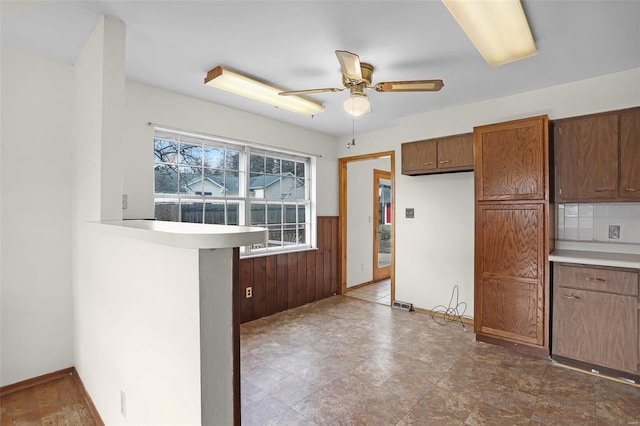 kitchen with tasteful backsplash, kitchen peninsula, ceiling fan, and wood walls