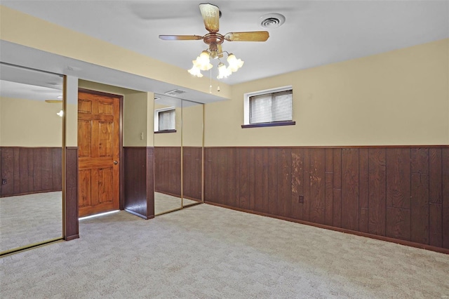 spare room featuring ceiling fan, light carpet, and wood walls