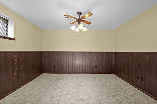 carpeted spare room featuring wooden walls and ceiling fan