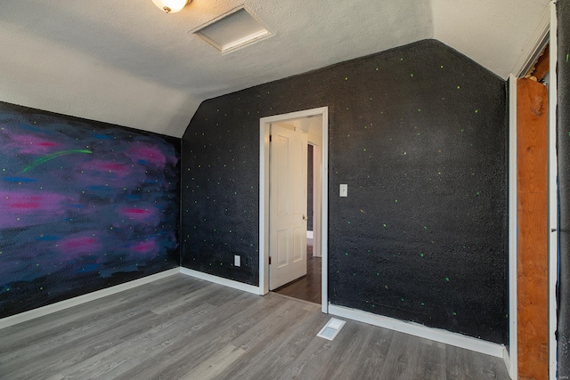 unfurnished bedroom featuring hardwood / wood-style flooring, vaulted ceiling, and a textured ceiling