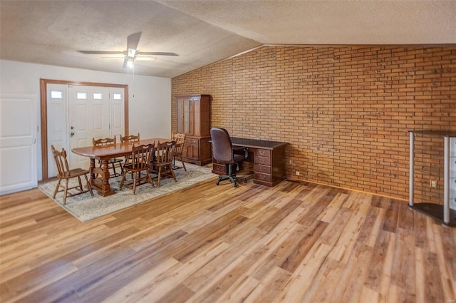 dining space with vaulted ceiling, brick wall, a textured ceiling, and light wood-type flooring