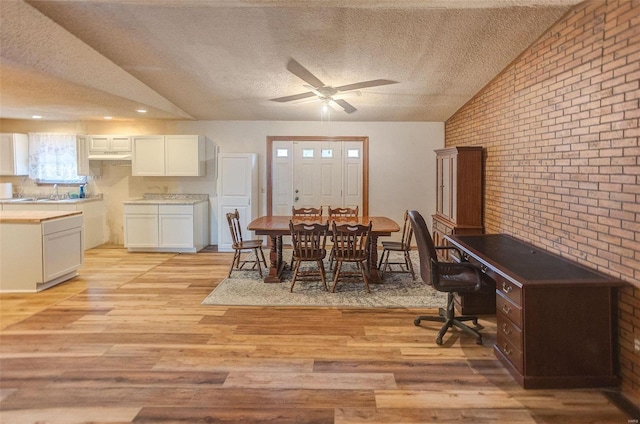 dining space with vaulted ceiling, a textured ceiling, ceiling fan, brick wall, and light hardwood / wood-style floors