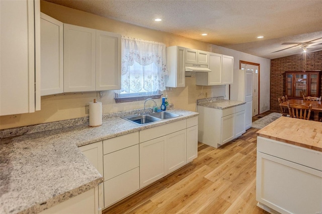 kitchen featuring brick wall, sink, white cabinets, a textured ceiling, and light hardwood / wood-style flooring