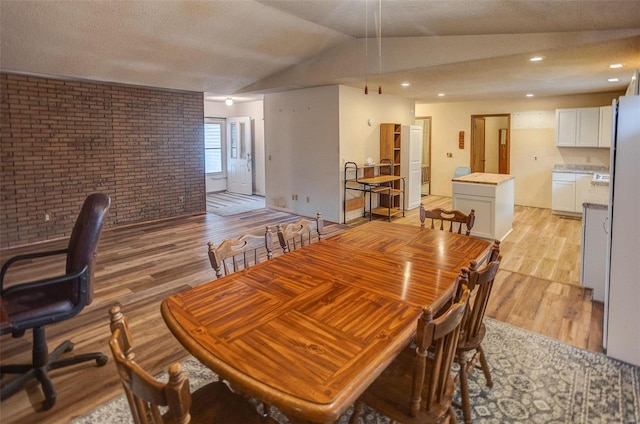 dining room with brick wall, lofted ceiling, a textured ceiling, and light wood-type flooring