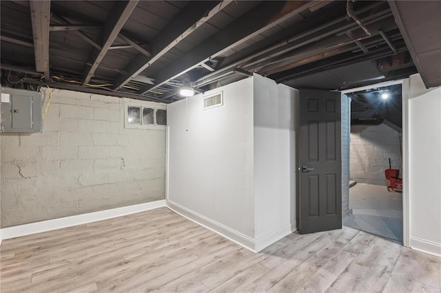 basement featuring electric panel and light hardwood / wood-style floors