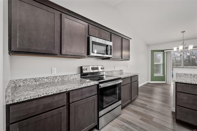 kitchen featuring light wood-style flooring, light stone counters, an inviting chandelier, stainless steel appliances, and dark brown cabinets