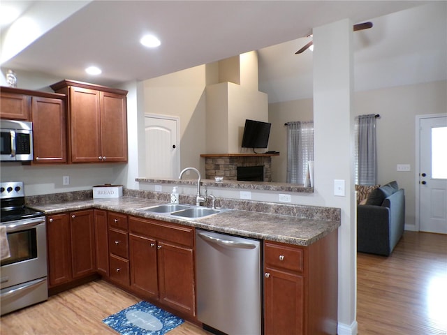 kitchen with lofted ceiling, sink, light hardwood / wood-style flooring, appliances with stainless steel finishes, and a fireplace