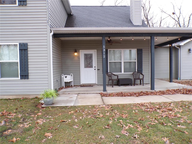 view of exterior entry featuring covered porch, roof with shingles, a lawn, and a chimney