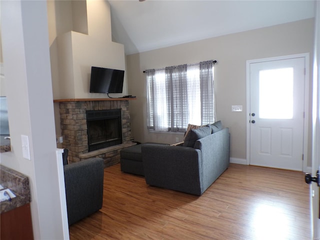 living room featuring vaulted ceiling, a stone fireplace, wood finished floors, and baseboards