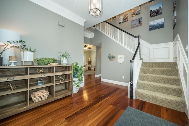 stairway with wood-type flooring, ornamental molding, ceiling fan, and a high ceiling