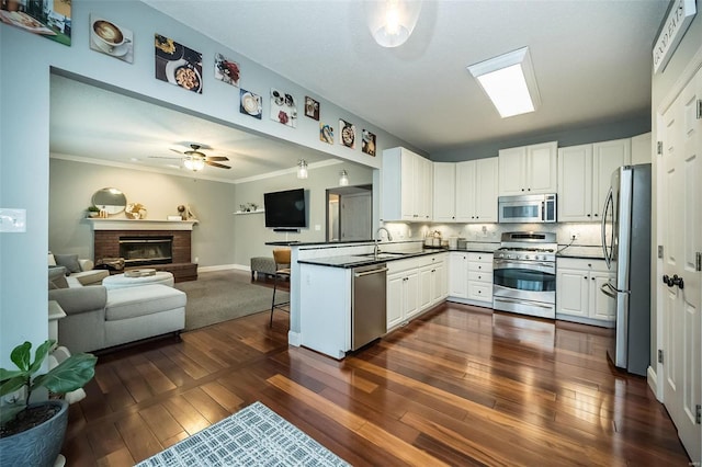 kitchen featuring dark wood-type flooring, appliances with stainless steel finishes, a fireplace, white cabinets, and kitchen peninsula