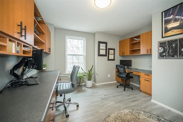 office space with built in desk, a textured ceiling, and light wood-type flooring