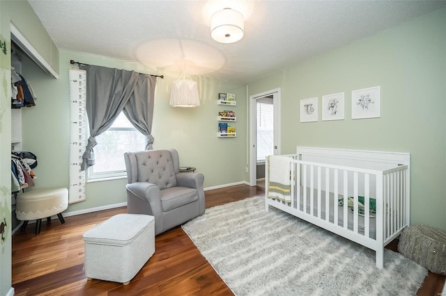 bedroom with hardwood / wood-style floors, a nursery area, and a textured ceiling