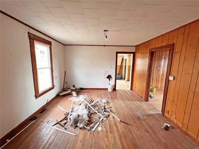 empty room with ornamental molding, light wood-type flooring, and wood walls