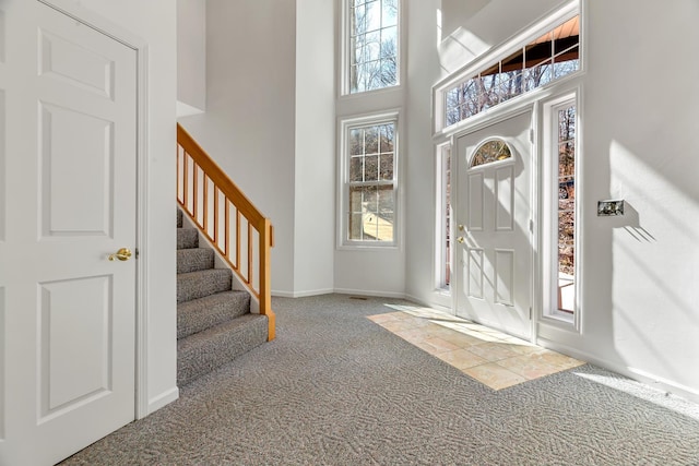 carpeted foyer entrance featuring baseboards, stairway, and a towering ceiling