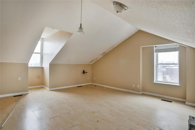bonus room featuring lofted ceiling, plenty of natural light, light hardwood / wood-style flooring, and a textured ceiling