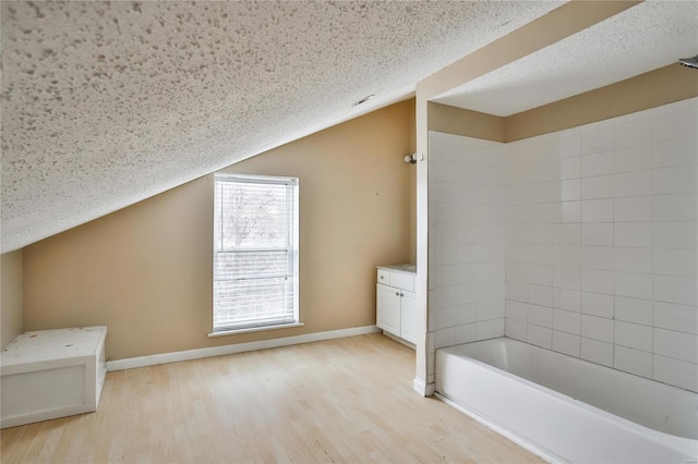 bathroom featuring lofted ceiling, hardwood / wood-style floors, tiled shower / bath combo, vanity, and a textured ceiling