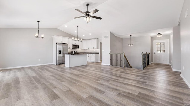 unfurnished living room with ceiling fan with notable chandelier, light hardwood / wood-style flooring, and vaulted ceiling