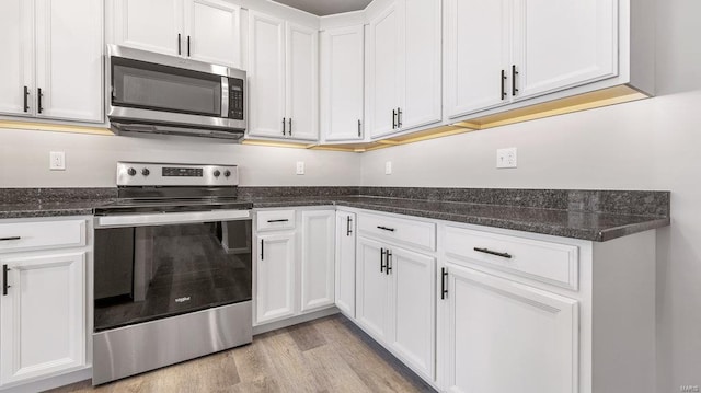 kitchen featuring white cabinetry, appliances with stainless steel finishes, dark stone countertops, and light wood-type flooring