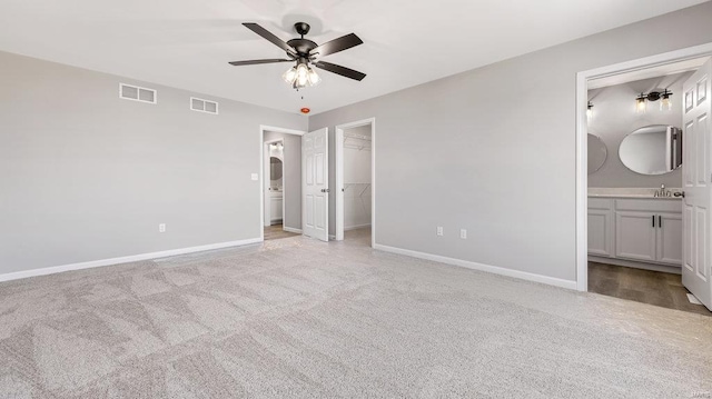 unfurnished bedroom featuring sink, ensuite bath, a spacious closet, light colored carpet, and a closet