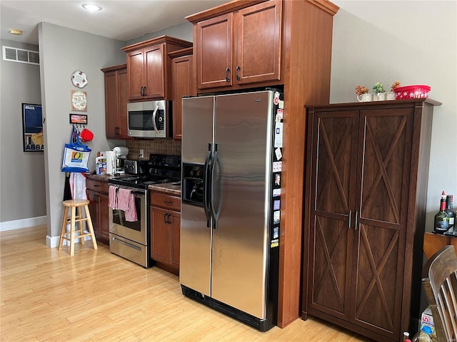 kitchen featuring decorative backsplash, appliances with stainless steel finishes, and light hardwood / wood-style flooring