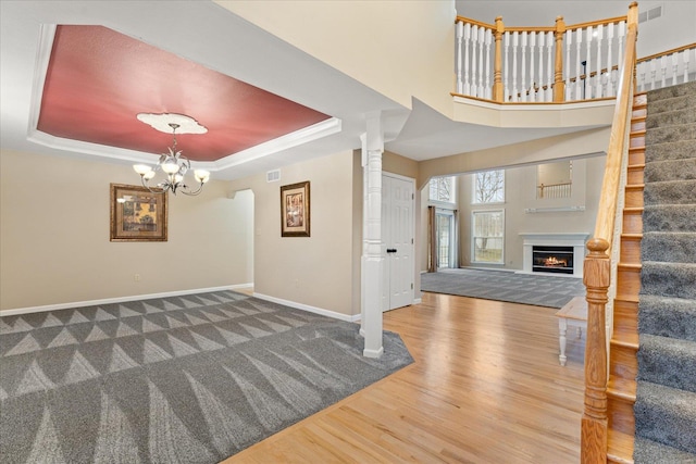 foyer entrance with a raised ceiling, hardwood / wood-style flooring, a notable chandelier, and ornate columns