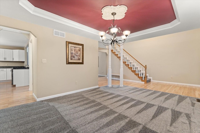 unfurnished living room featuring an inviting chandelier, ornamental molding, a tray ceiling, and light wood-type flooring