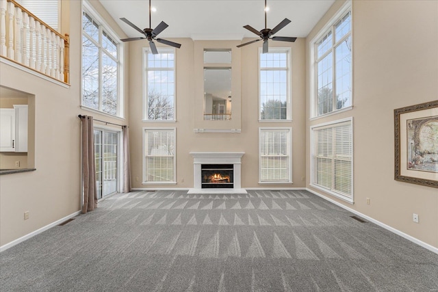 unfurnished living room with a towering ceiling, ceiling fan, and carpet