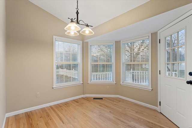 unfurnished dining area featuring lofted ceiling, a chandelier, and light wood-type flooring