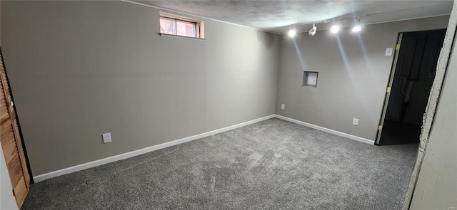 basement with rail lighting and dark colored carpet