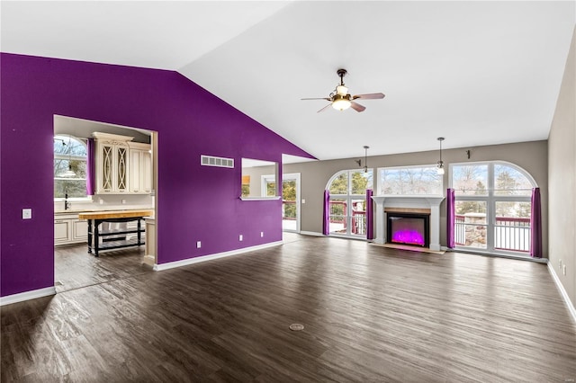 unfurnished living room featuring dark hardwood / wood-style flooring, a healthy amount of sunlight, vaulted ceiling, and ceiling fan