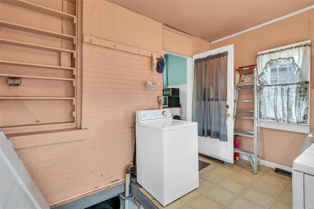 clothes washing area with a healthy amount of sunlight, brick wall, and washer / dryer