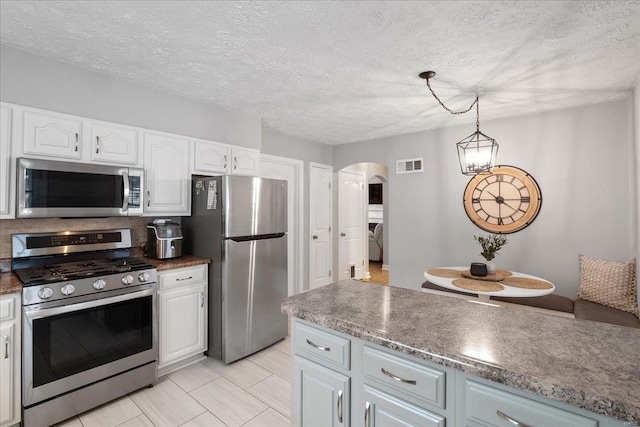 kitchen featuring white cabinetry, hanging light fixtures, a textured ceiling, appliances with stainless steel finishes, and decorative backsplash