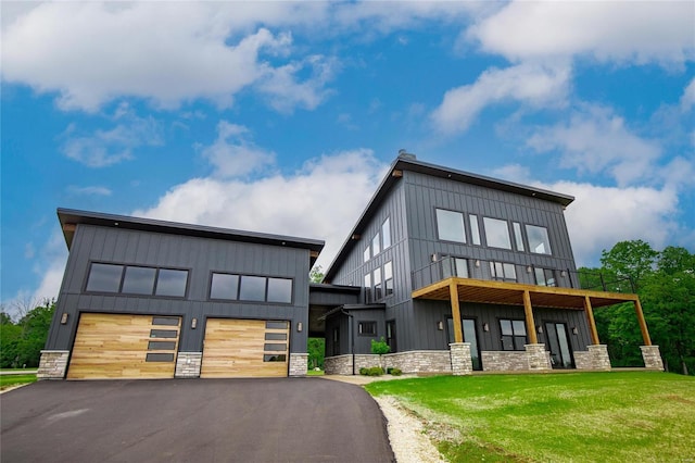 modern home with board and batten siding, aphalt driveway, a garage, and stone siding