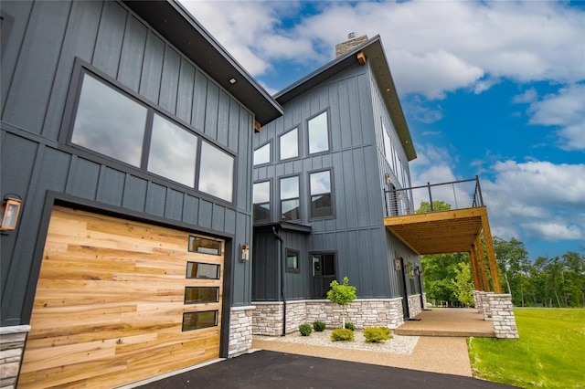 exterior space with stone siding, board and batten siding, a chimney, and a garage