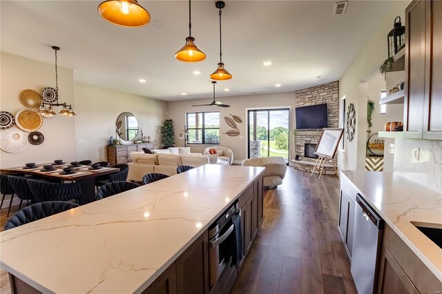 kitchen with decorative light fixtures, appliances with stainless steel finishes, dark hardwood / wood-style floors, a fireplace, and light stone countertops